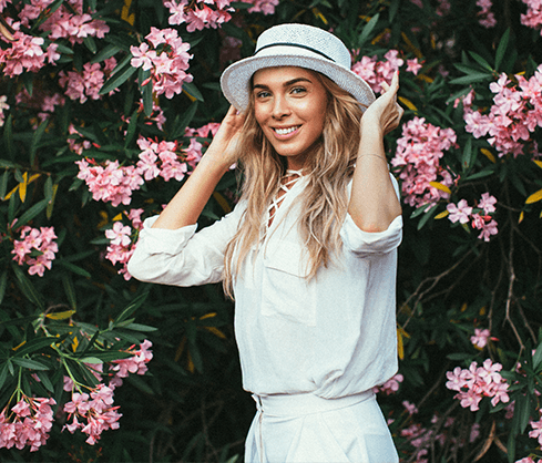 woman with hat on in front of flowers