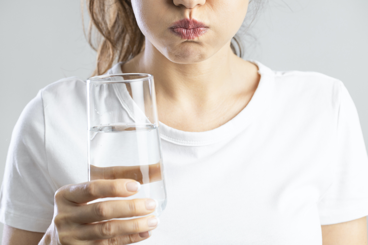 Closeup of a woman in a white shirt rinsing with water to ease her dry mouth