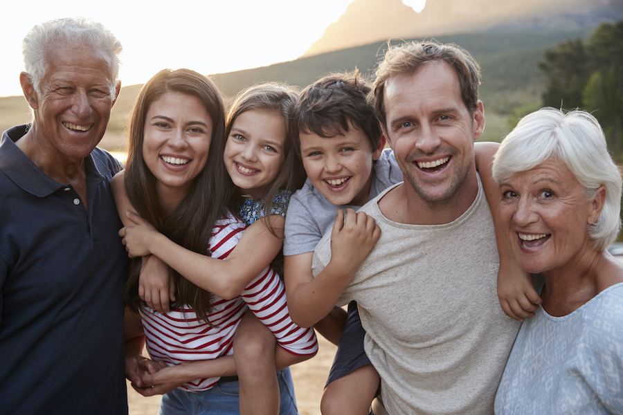 Multigenerational family of grandparents, parents, and 2 children smiling outside