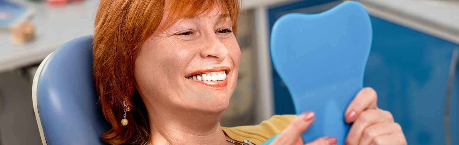 woman sitting in dental chair and admiring her smile in a mirror