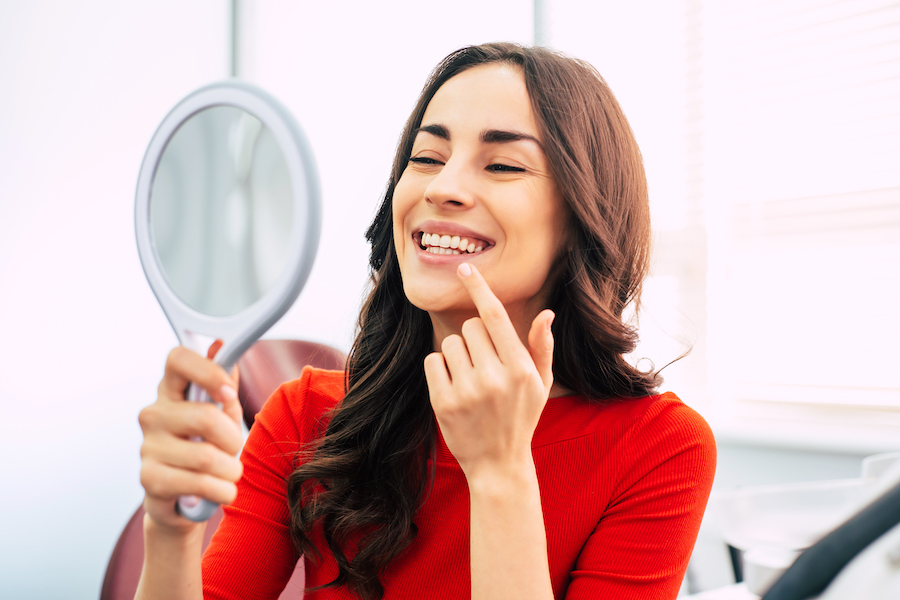 Photograph of woman in dental chair smiling at her teeth after cosmetic dentistry.