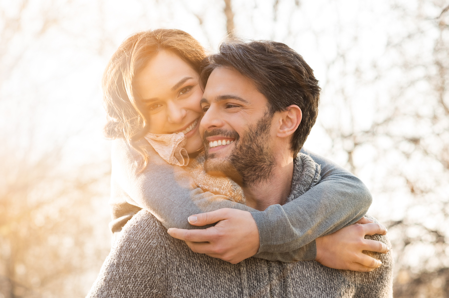 cosmetic dentistry services, cosmetic dentistry, couple smiling in sweaters, Closeup of smiling man carrying woman piggyback outdoor