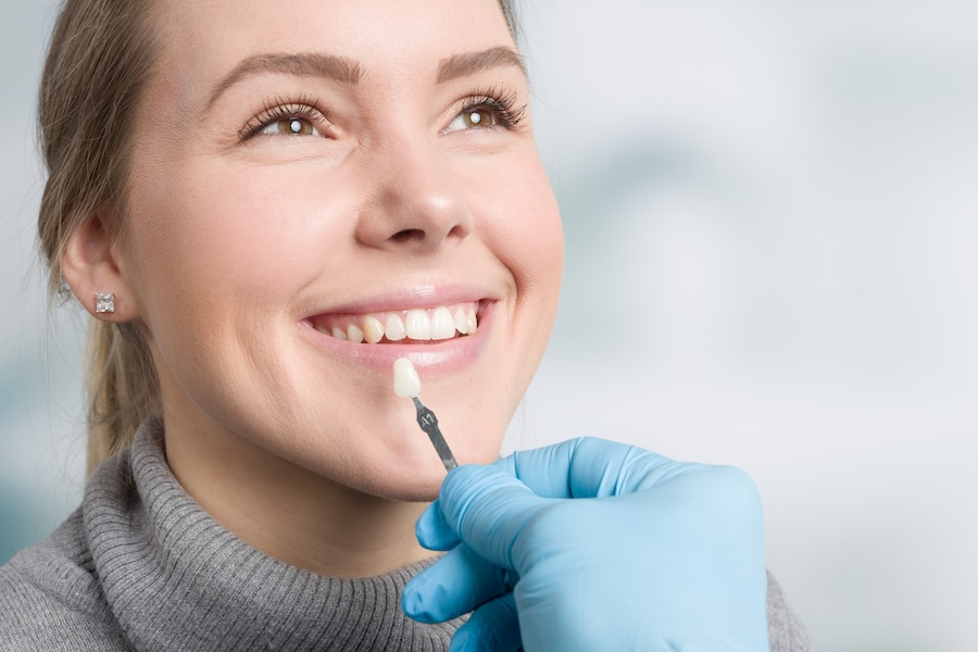 woman using shade guide to decide between veneers or teeth whitening