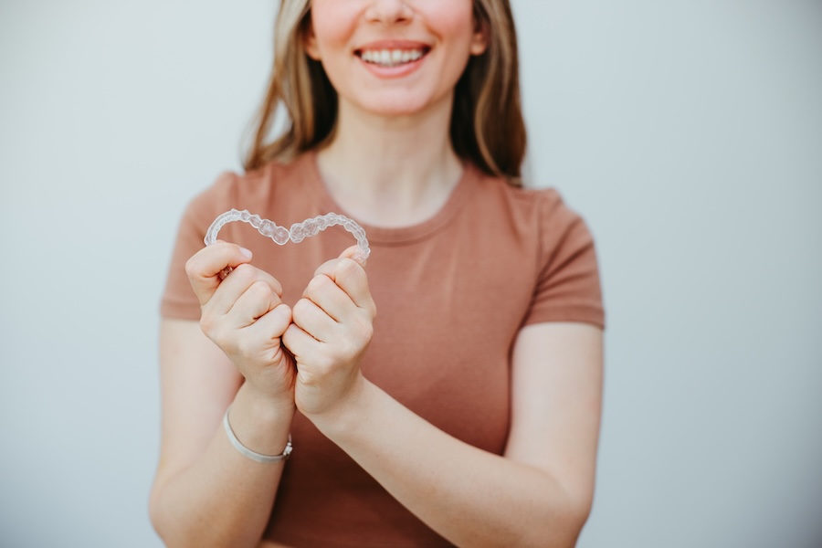 woman holding invisalign clear aligners to straighten teeth before fall