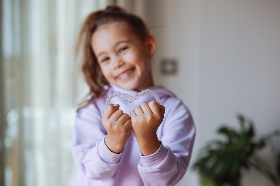 child holding invisalign trays in a heart shape can you get invisalign with baby teeth